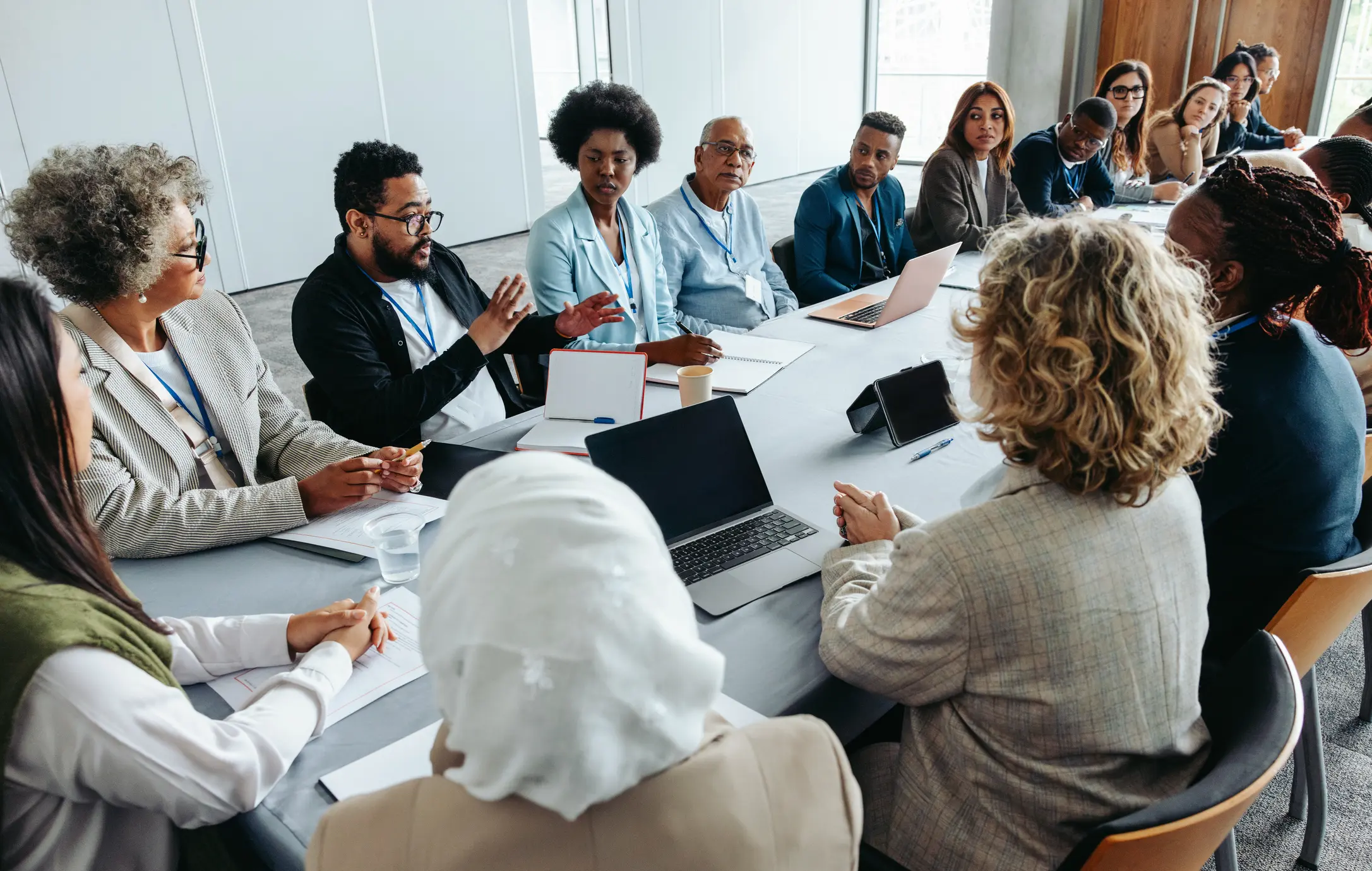 People at a conference table discussing something. Various ethnicities are depicted.